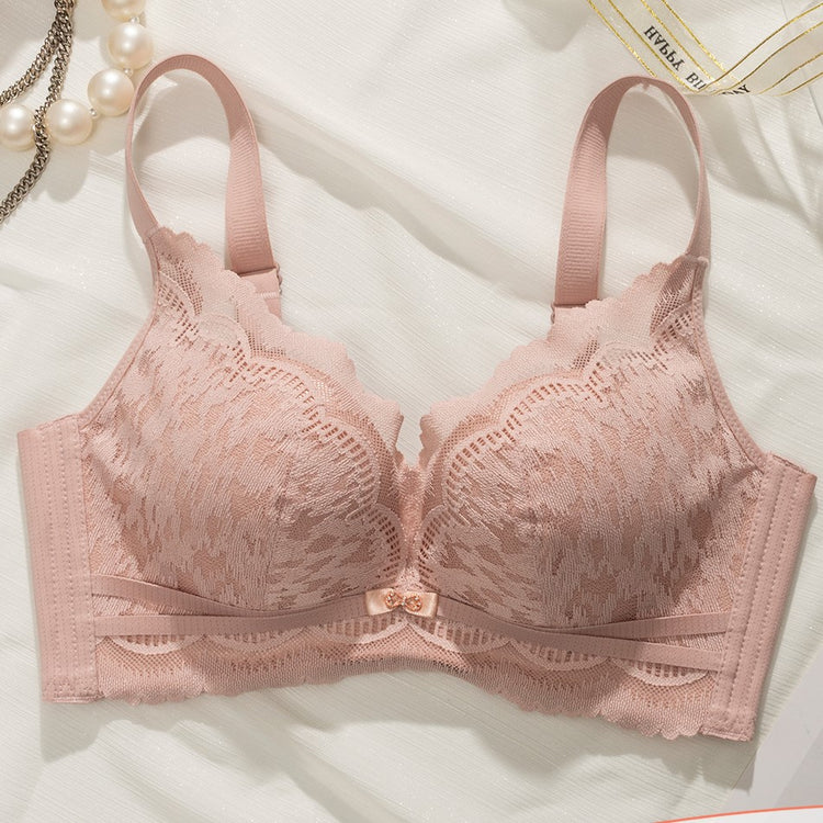 Flat lay of a pink Chic Lace Wireless Push-up Bra, featuring delicate lace patterns and a bow accent in the center, placed on a light fabric background with pearl accents.