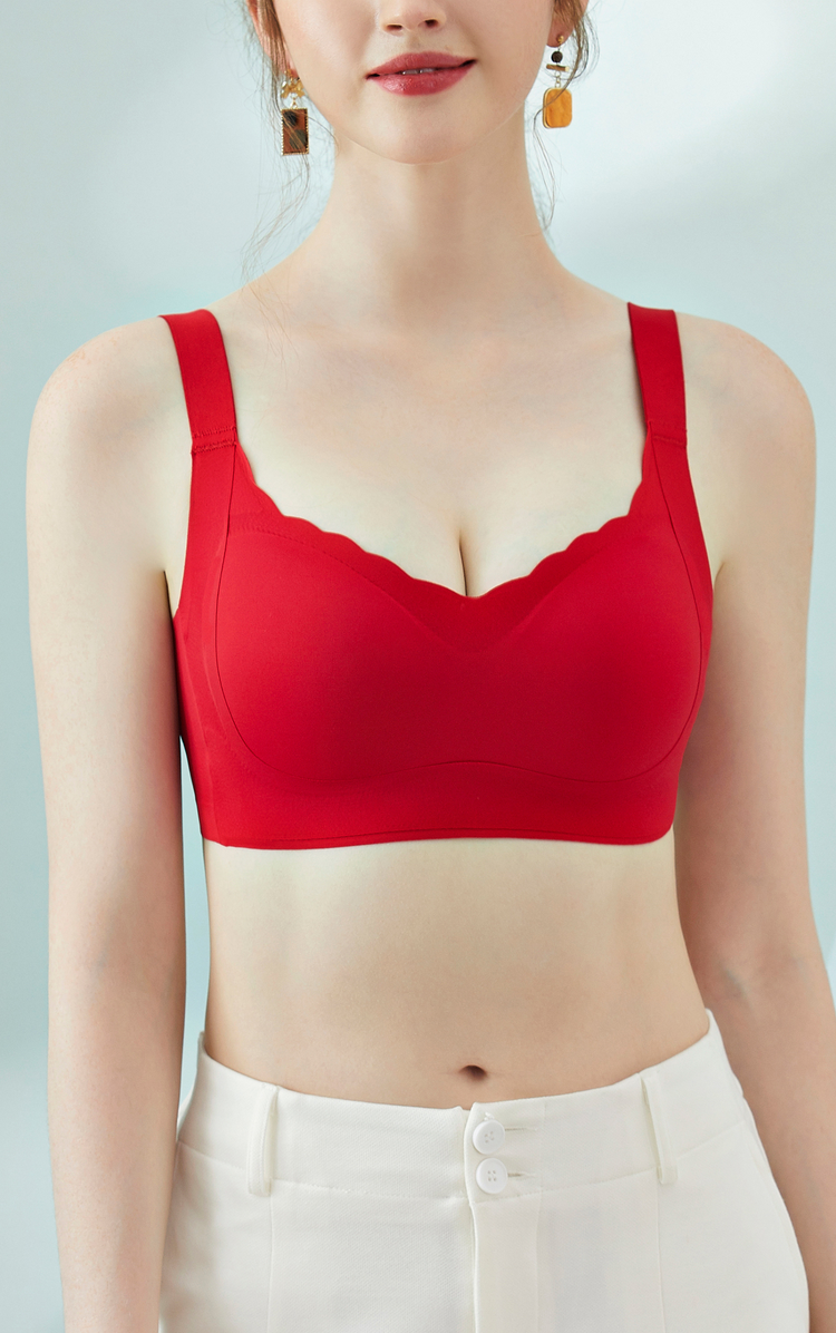 A front view image of a model wearing a red wireless bra with scalloped edges and wide shoulder straps, paired with white pants.