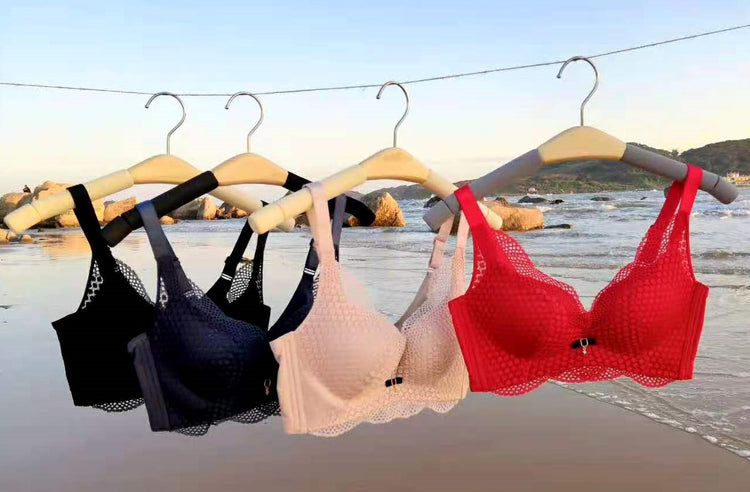 Black, gray, beige, and red lace push-up bras hanging on wooden hangers by the beach, showcasing their stylish design and color variety.